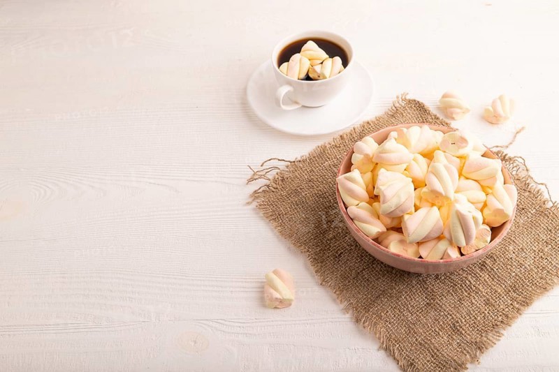 Orange and pink marshmallow in ceramic bowl on white wooden background and linen textile, side view, copy space, minimalism