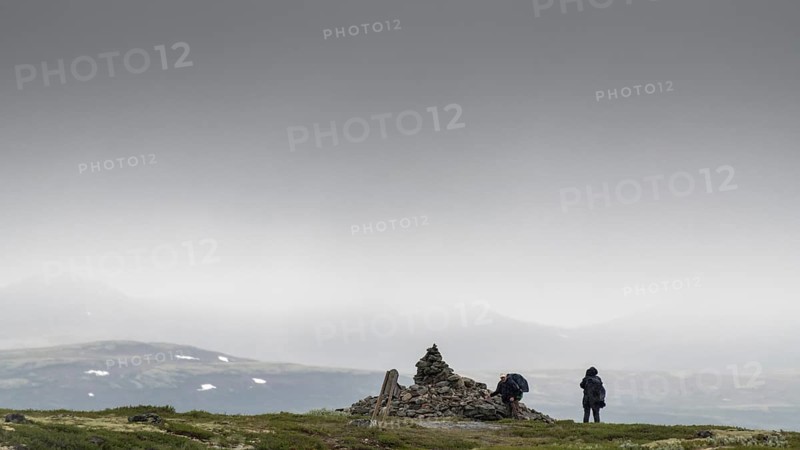 Two pilgrims lay stones at the stone pyramid Allmannrøysa, cloudy landscape, pilgrimage route Olavsweg or Olavsleden, old Kongevegen or King's Path over the Dovrefjell, Norway
