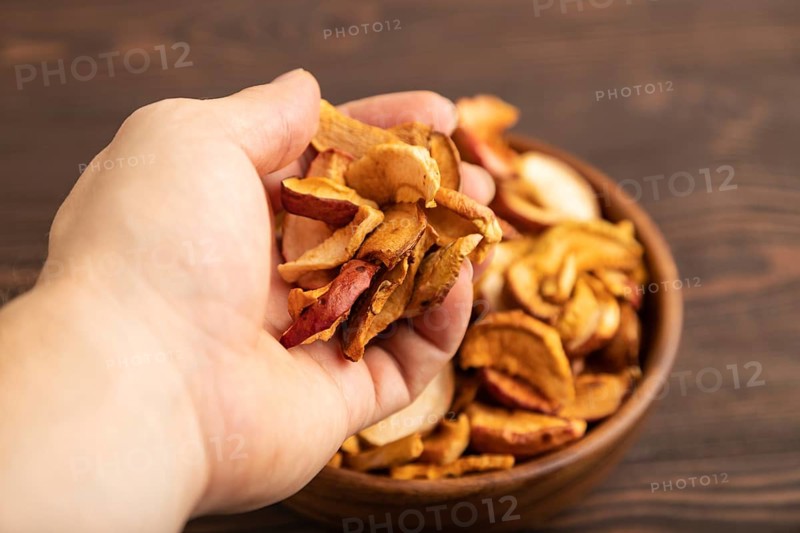 Dried Apples in wooden bowl with hand on brown wooden background. Side view, close up, healthy food, minimalism. sweet, selective focus