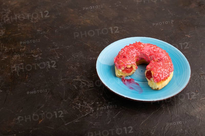 Bitten Pink Donut with sprinkles on blue ceramic plate on black concrete background, side view, copy space, minimalism