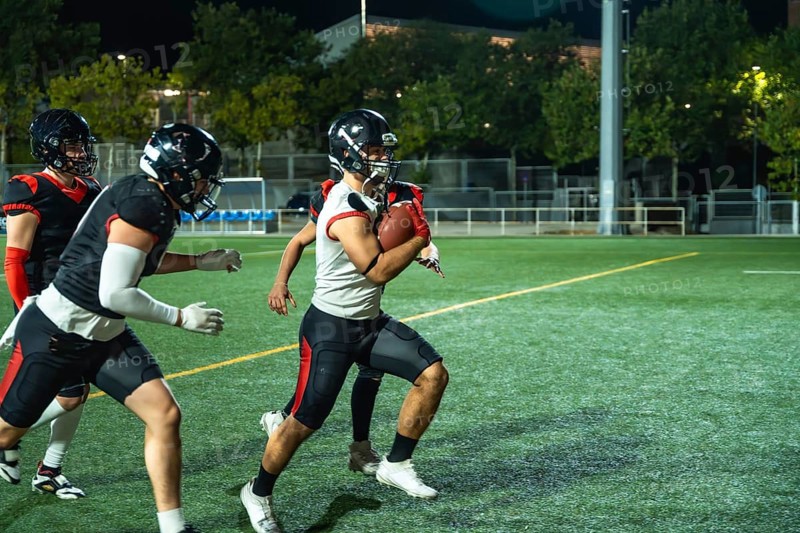 American football player is running with the ball, while teammates are blocking opponents during an intense game on a floodlit artificial turf field under the night sky