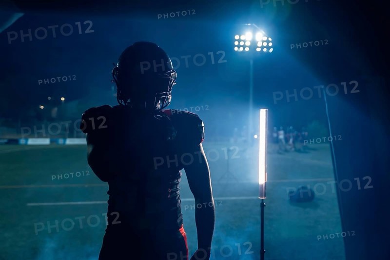 Football player standing in silhouette, ready to enter the stadium field at night, stadium lights creating a dramatic atmosphere, preparing for the game, showing determination