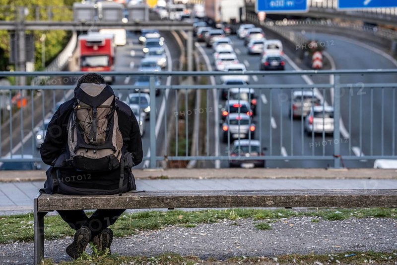 Man sitting on a bench, looking at the traffic jam on the A40 motorway, Ruhrschnellweg, in the city passage of Essen, at Europaplatz, entrance to the Ruhrschnellweg tunnel, North Rhine-Westphalia, Germany