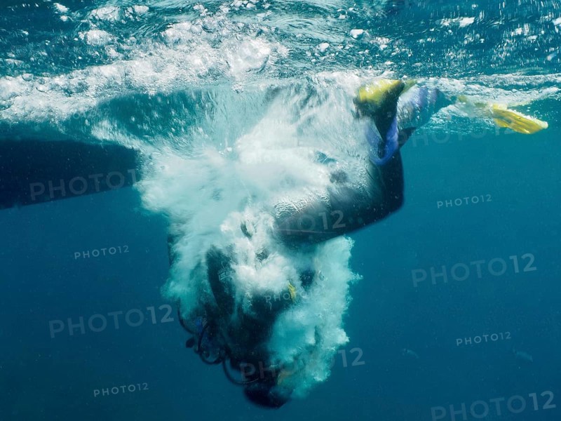 Eine Taucherin ist mit einer Rolle rückwärts vom Boot gesprungen und bricht durch die Wasseroberfläche, um ins Meer einzutauchen. Tauchplatz Muzil, Stoja, Pula, Kroatien, Mittelmeer
