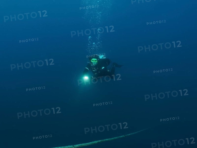 Ein Taucher mit Lampe steigt aus der dunklen Unterwasserwelt auf, einem Seil folgend. Tauchplatz Wrack der Giuseppe Dezza, Pula, Kroatien, Mittelmeer