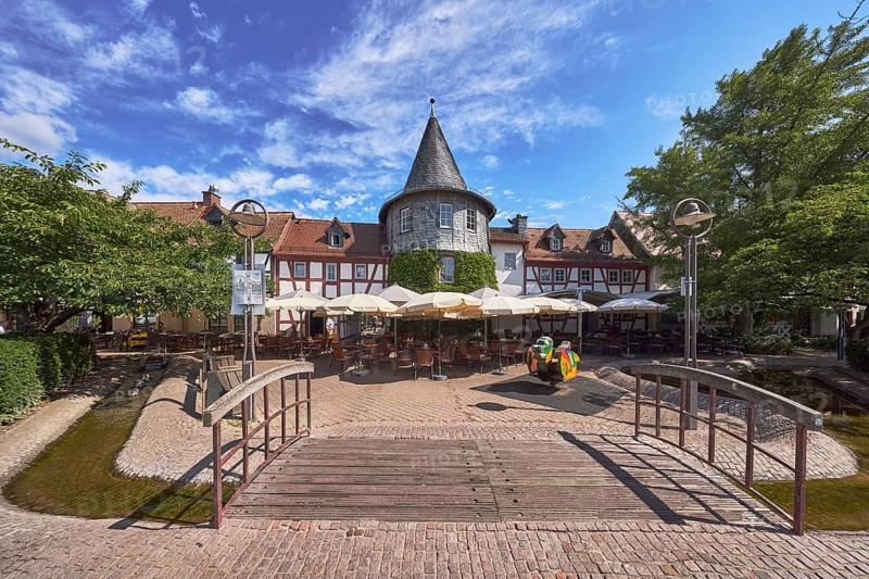 Fachwerkhäuser, Turm, Häuserzeile, Fußgängerbrücke, Holzbrücke, hölzern, Altstadt, historische Gebäude, Gehweg aus Klinker, Pflastersteine, Restaurant Zum Türmchen, Außenbereich einer Gastronomie mit Sonnenschirmen, Tischen und Stühlen, blauer Himmel, Cumuluswolken, Cirrostratuswolken, Platz am Untertor, Burggrabenstraße, Hofheim am Taunus, Main-Taunus-Kreis, Hessen, Deutschland