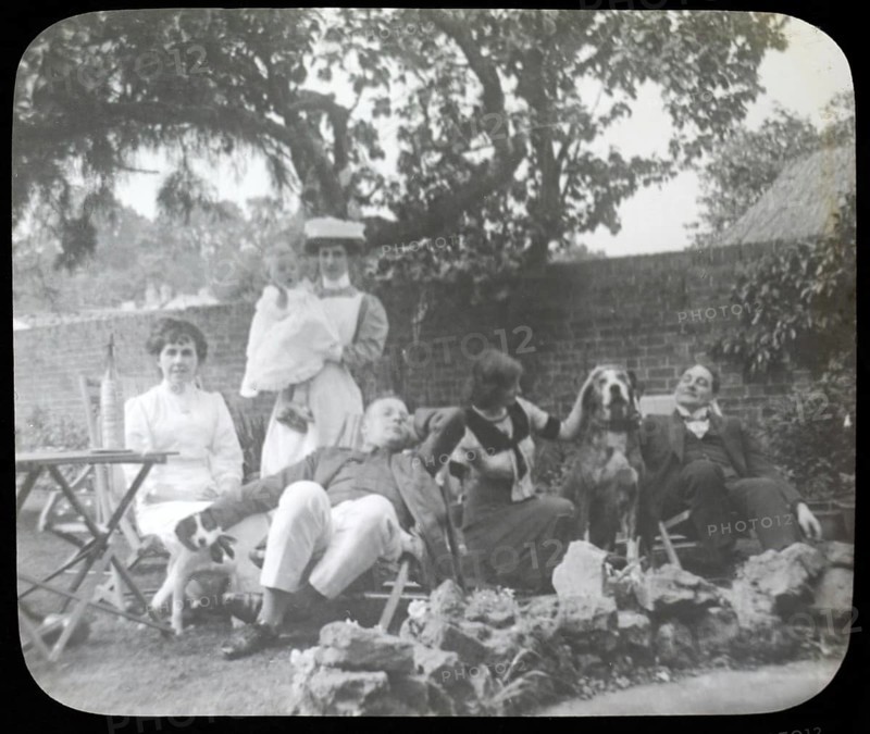 Affluent Edwardian family group men and women with nursemaid holding baby, outdoors in garden sitting in deckchairs with dogs, England, Uk, 1900 - 1930s