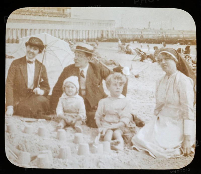Affluent Edwardian family sitting on sandy seaside beach man, woman, children with nursemaid England, UK, 1900 - 1930s