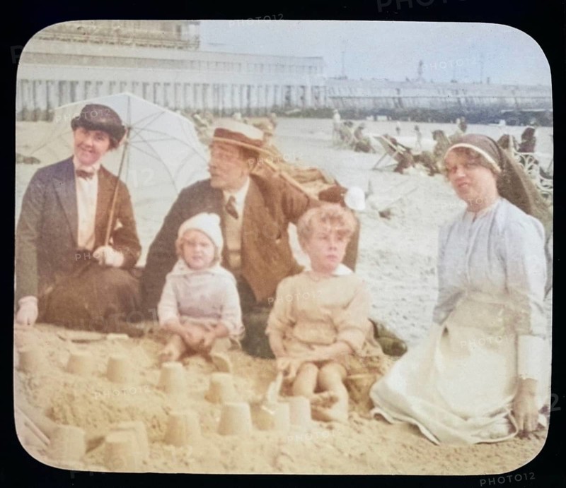 Affluent Edwardian family sitting on sandy seaside beach man, woman, children with nursemaid England, UK, 1900 - 1930s colourised