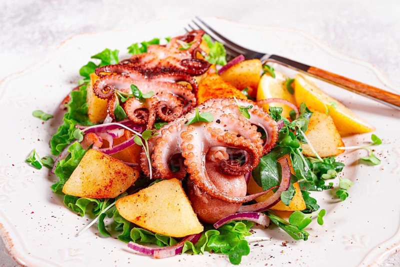 Grilled octopus with baked potatoes and fresh herbs, on a decorative light plate, homemade, no people