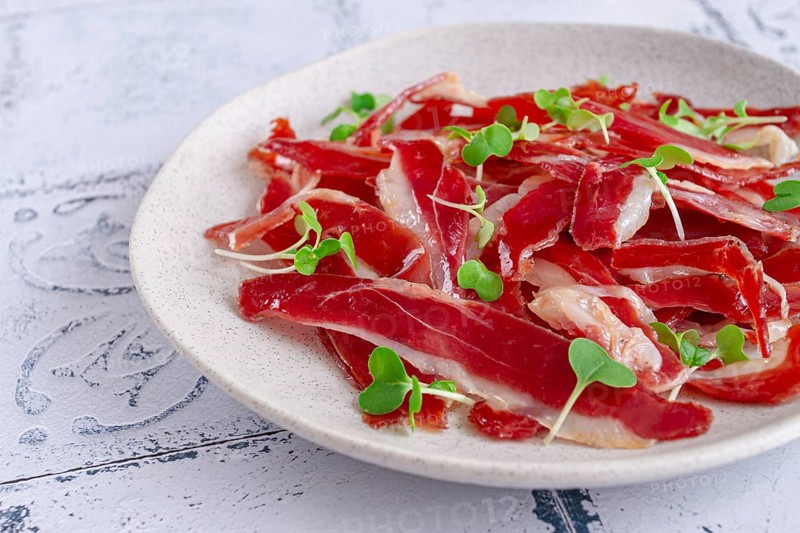 Ham of duck breast, dried duck fillet, with microgreens, plate, on a tiled table