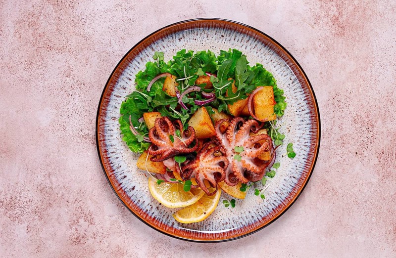 Grilled octopus with baked potatoes and fresh herbs, on a decorative plate, homemade
