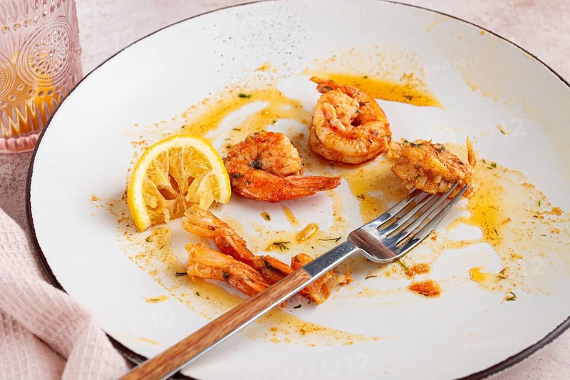 The remains of fried shrimp in oil with spices, on a white plate, with a fork, there are no people