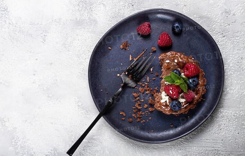 Half-eaten chocolate tartlet, on a plate, stuffed with cottage cheese and berries, breakfast, homemade, no people