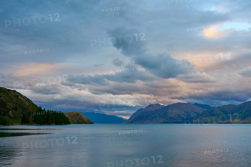 Friedlicher See mit Bergpanorama und bewölktem Himmel kurz vor Sonnenuntergang, Lake Hawea, Hawea, Otago, Südinsel, Neuseeland
