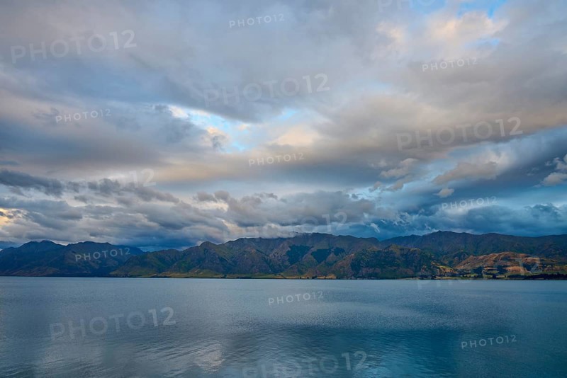 Stilles Gewässer vor bergiger Landschaft und dramatischem Himmel in der Dämmerung, Lake Hawea, Hawea, Otago, Südinsel, Neuseeland