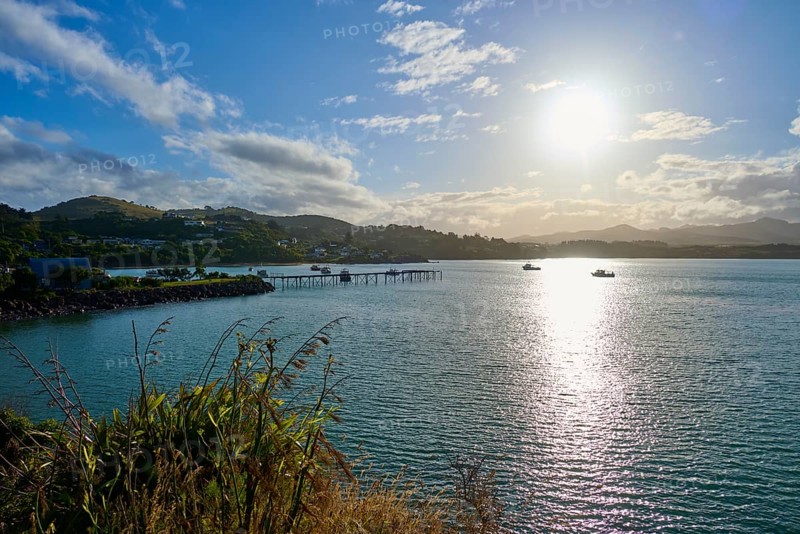 Das Sonnenlicht reflektiert auf dem Meer mit Booten und einem Pier, Moeraki, Hampden, North Otago, Südinsel, Neuseeland