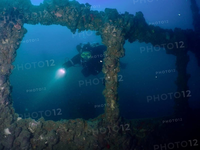 A diver explores the windows of a shipwreck with a lamp. Dive site wreck of the Baron Gautsch, Pula, Croatia, Mediterranean Sea
