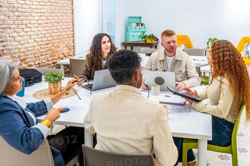 Diverse business professionals working together around a table, sharing ideas and analyzing data with laptops and a tablet during a business meeting in a modern office space