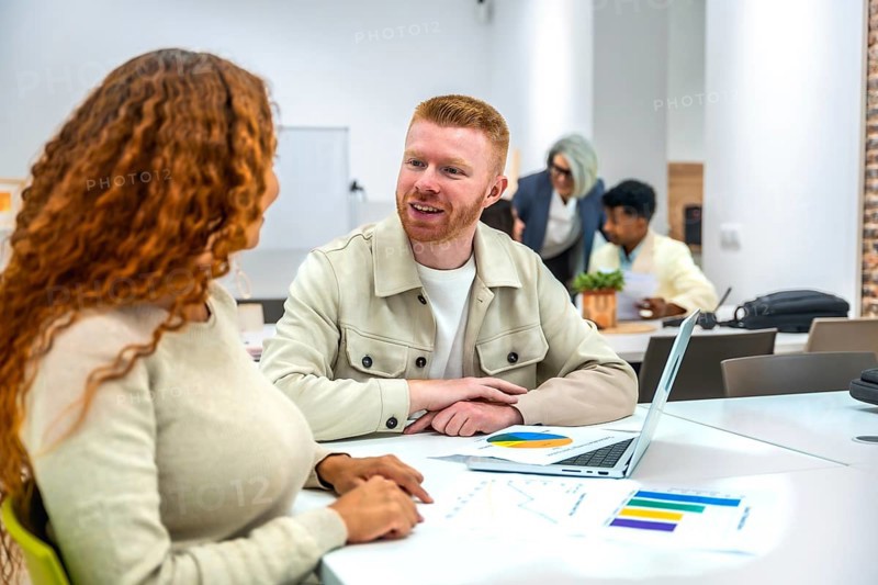 Diverse colleagues collaborate over charts and laptops in a modern coworking space, sharing ideas, analyzing data and planning strategy during an informal, creative meeting