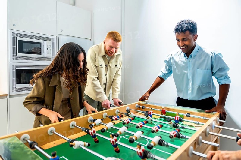 Diverse coworkers enjoying a friendly foosball game during a work break, fostering teamwork, camaraderie, and a positive office environment in a modern workplace
