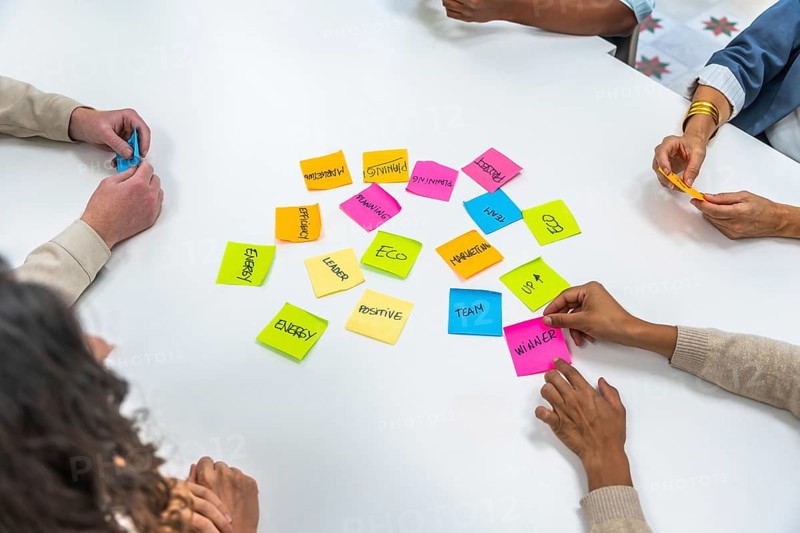 Diverse business people collaborating in a meeting, brainstorming new concepts for strategy, planning, and project development using colorful sticky notes on a white table
