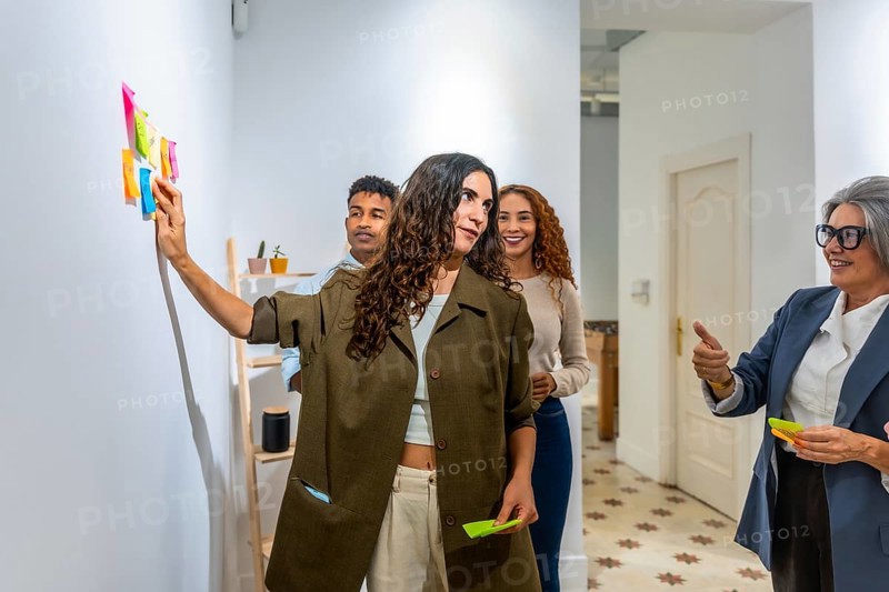Diverse business team collaborating and brainstorming ideas, using colorful sticky notes on a wall during a creative strategy meeting in a modern office environment