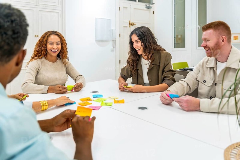 Multicultural colleagues collaborating in a modern office workshop, arranging colorful sticky notes on a white table while brainstorming ideas, planning projects and fostering innovation