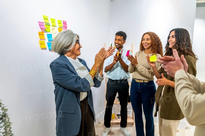 Diverse business people clapping hands in an office meeting room, celebrating a successful project achievement or a senior female manager's accomplishment, demonstrating teamwork and appreciation