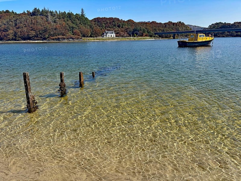 Clear lake surface with a yellow boat and wooden houses on the shore, Silver Sands of Morar, Morar, Scotland, United Kingdom