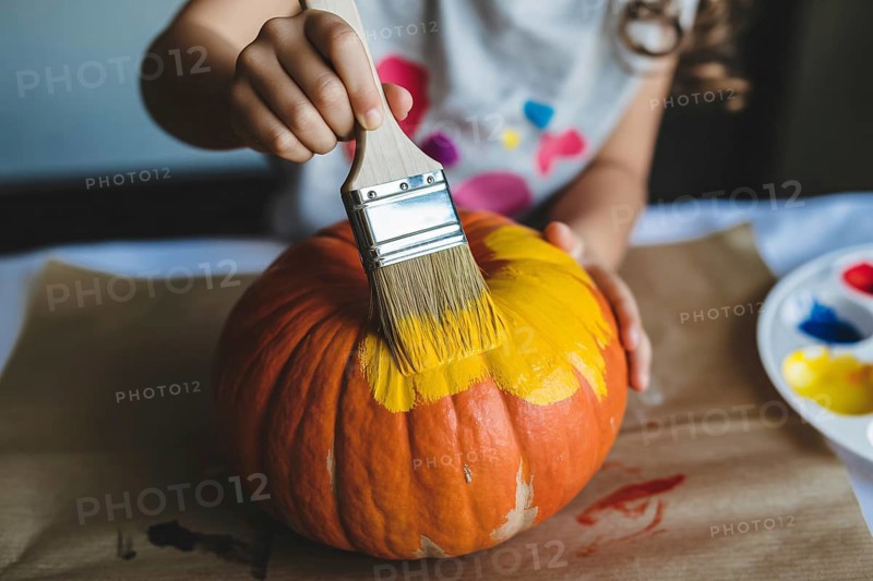 Close up of orange Halloween pumpkin being painted yellow by a child, AI generated