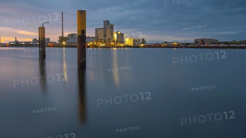 View across the Weser past dolphins to an industrial area in the evening light, Gröpelingen, Bremen, Germany