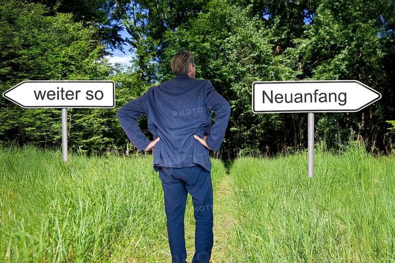 (Photomontage) Businessman stands in nature and has the choice between the direction CONTINUE AS IS and the direction NEW BEGINNING