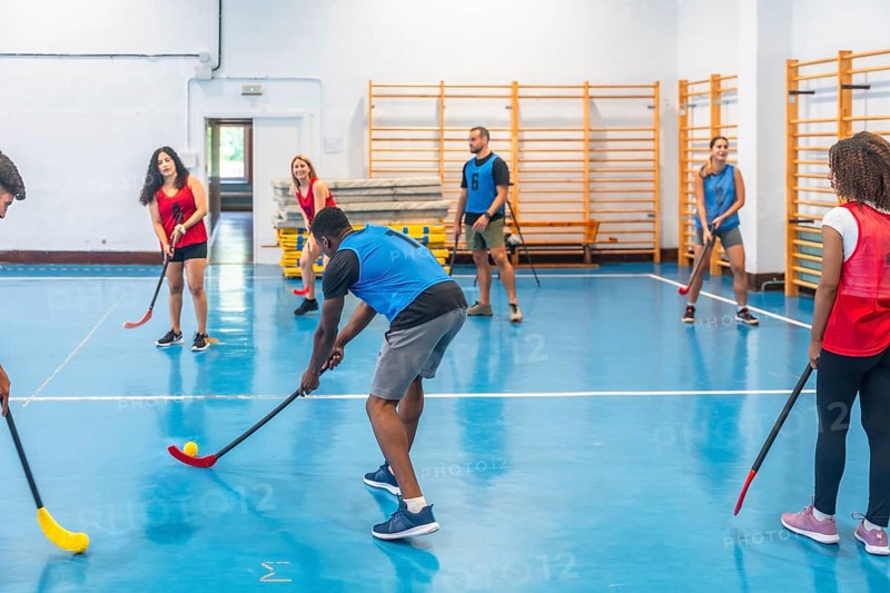Floorball team players practicing passes during training inside a gym, skillfully hitting the ball with their sticks on the vibrant blue floor, showcasing teamwork and athleticism