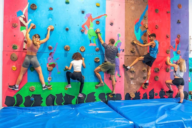 Five athletes climbing a bouldering wall in a gym, focusing on their training and exercising together to enhance their climbing skills while enjoying a fun and active experience