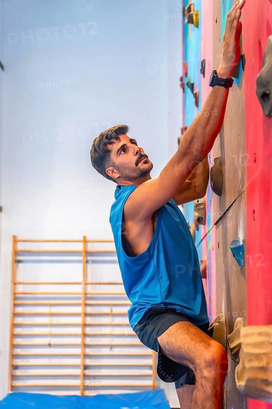 Concentrated male athlete meticulously gripping colorful handholds while ascending an artificial rock climbing wall, demonstrating strength, agility, and focus in an indoor gym environment