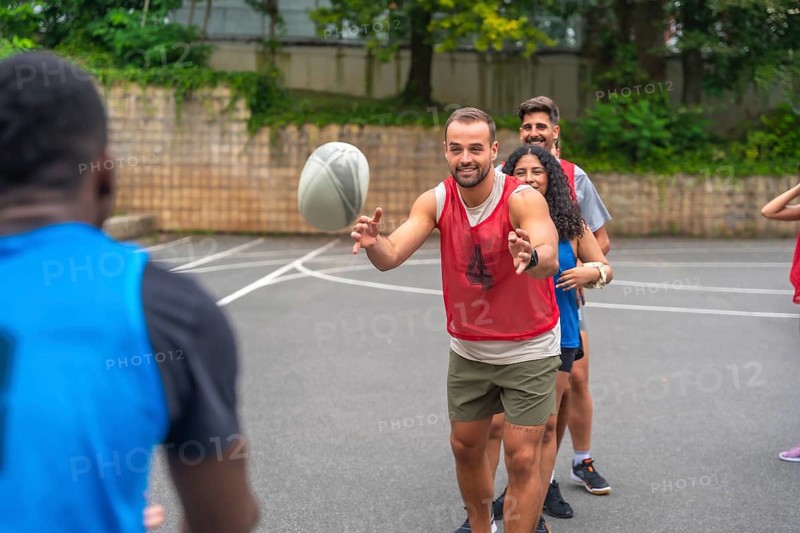 Group of athletes passing a rugby ball during a training session on an urban basketball court, practicing their skills and teamwork for an upcoming match