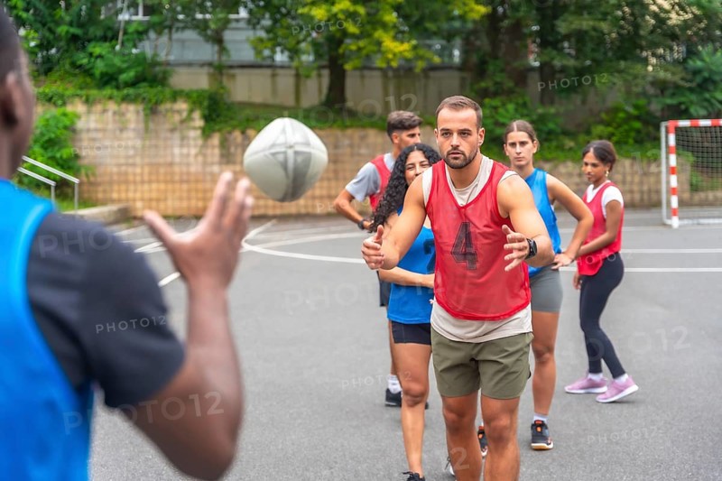 Multi ethnic rugby players engaging in passing drills on an outdoor court within a city park, fostering teamwork, promoting fitness, and exemplifying sportsmanship among athletes