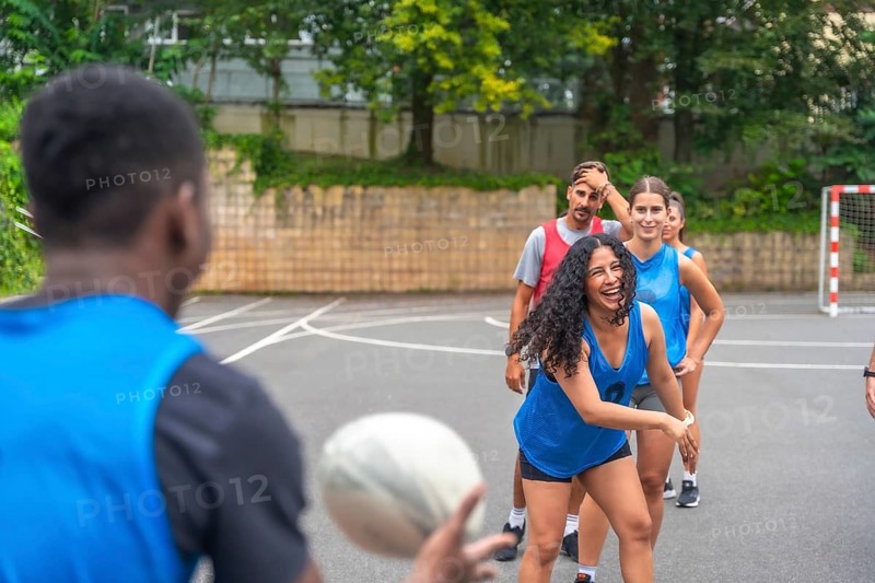 Diverse group of multi ethnic rugby players enjoying training on an outdoor court, passing the ball with enthusiasm and showcasing the joy of teamwork and camaraderie in the sport