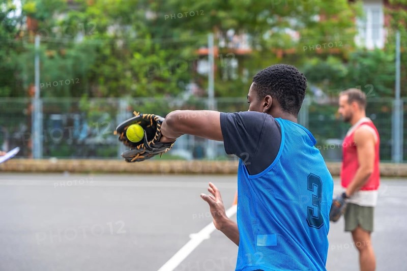 Young baseball player wearing a blue uniform is pitching the ball with his glove during a game on the field while another player waits in the background