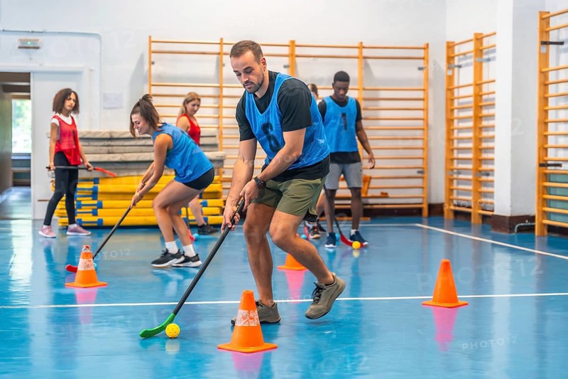 Group of athletes engaging in floorball practice, running with sticks and skillfully hitting the ball during an intense training session inside a gym environment