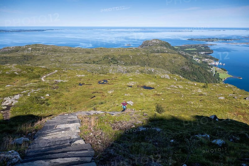 Woman with backpack climbing up stone stairs, Sherpat stairs or Midsund stairs or Midsundtrappene, Bløkallen hike, in the background sea and islands, island Otroya or Otrøya, Møre og Romsdal, Norway