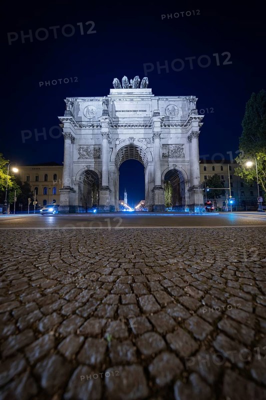 Night shot of the illuminated Siegestor on cobblestone street, Siegestor, Munich, Germany