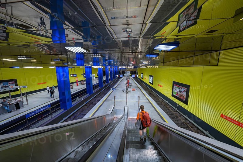 Modern underground station with yellow walls and escalator, people in the hall, Münchner Freiheit, Munich, Germany