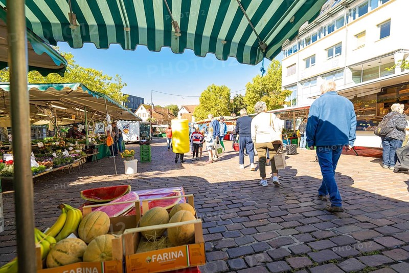 Visitors under striped market umbrellas stroll past a stall with melons and bananas, Sindelfingen, Böblingen district, Germany