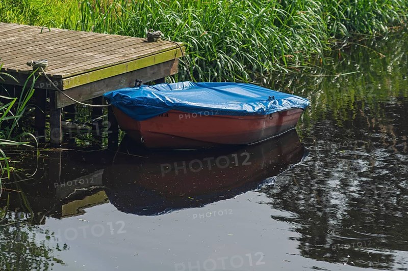Red plastic boat with blue tarpaulin, Lower Saxony, Germany