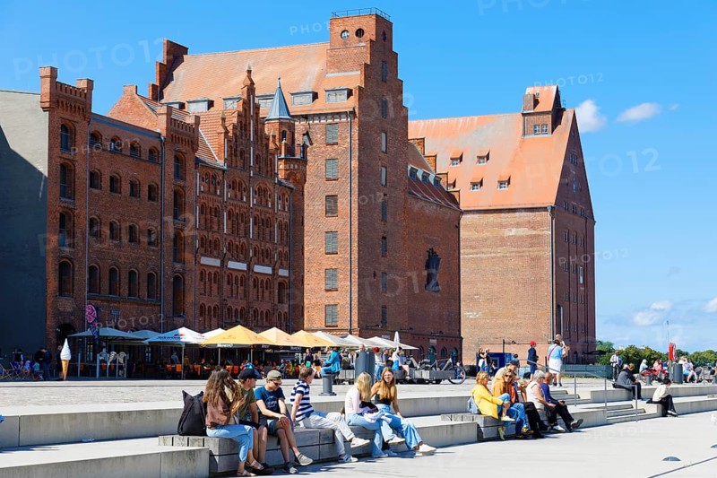 Visitors sitting and strolling along the waterfront promenade, warehouse building in the background, brick building, Hafenstraße, harbour island, Old Town, UNESCO World Heritage Site, Hanseatic City of Stralsund, Mecklenburg-Western Pomerania, Germany