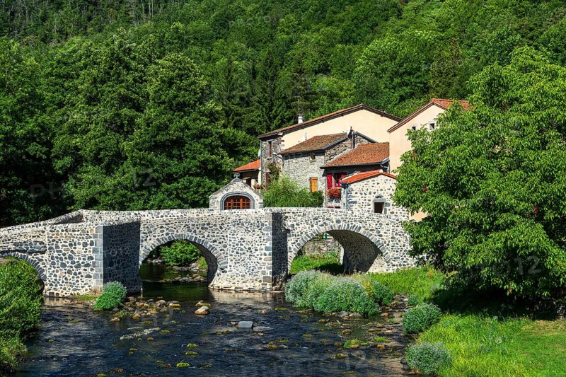 Stone bridge over the Pavin couze river flowing through the village of Saurier, Puy de Dome. Auvergne Rhone Alpes, France