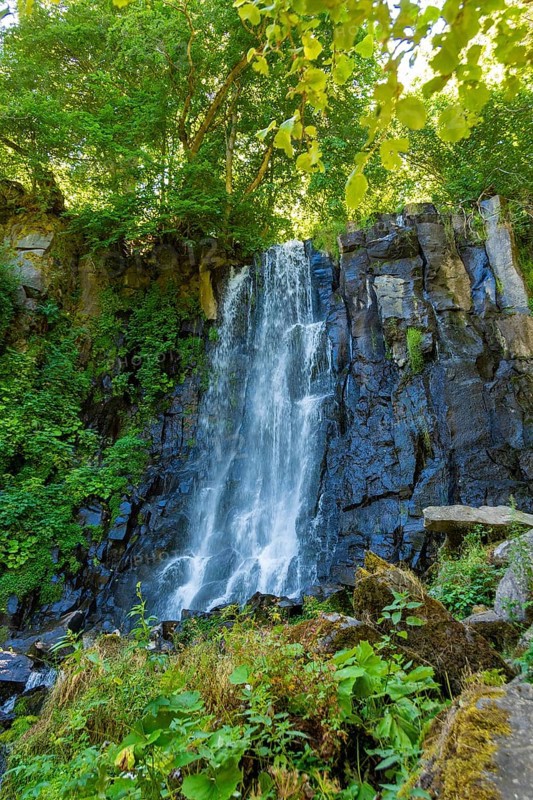 Vaucoux waterfall cascades gracefully over dark rocks, surrounded by lush greenery, Auvergne Volcanoes Regional Park, Puy de Dome., Auvergne-Rhone-Alpes, France