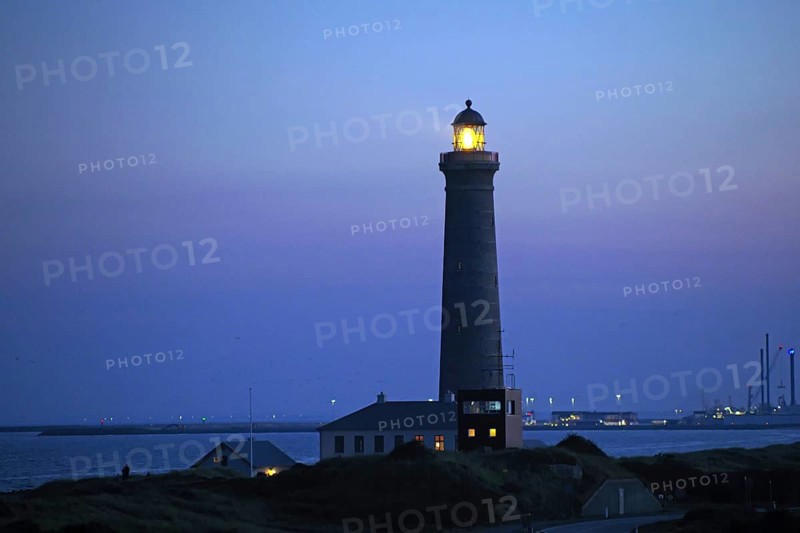 A lighthouse shines at dusk on the coast, surrounded by calm sea and blue sky, Skagen, Denmark